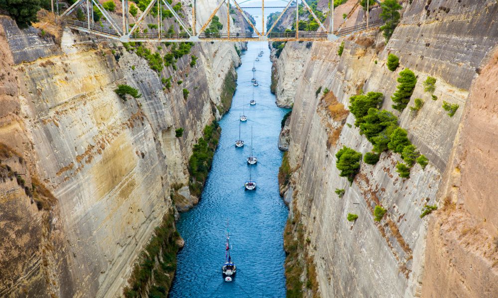 1. Corinth Canal
Visiting the Corinth Canal is probably one of the most important things to do in Corinth if you're a history lover. This Canal actually cuts through the Isthmus of Corinth, a small piece of land that connects mainland Greece to the Peloponnesus Peninsula (linking the Aegean Sea with the Ionian Sea). Its construction started in 1882 and was completed in 1893. This man-made waterway was built to save ships from having to pass around the peninsula.
Today, the Corinth Canal is one of the major tourist attractions in Corinth. Visitors come from around the world to experience the beautiful views of the surrounding area. The Canal is 6.4 km long, 21 meters wide, and 8 meters deep with rocky sides. The best view is definitely from the bridge that carries a road over it, where you can see both sides of the Canal.
One of the most interesting things to do here is actually getting out on the water. It's possible to take a boat ride through the Canal, which is definitely one of the highlights of any trip to Corinth. As you pass through this man-made wonder, you will see spectacular views of rocky sides and blue seas.
The area around the Canal is also quite picturesque, with panoramic views of the Isthmus and sardonic Gulf. I recommend taking a short hike to enjoy these amazing sights or just relax on the beach below. It's an excellent place for hiking.
